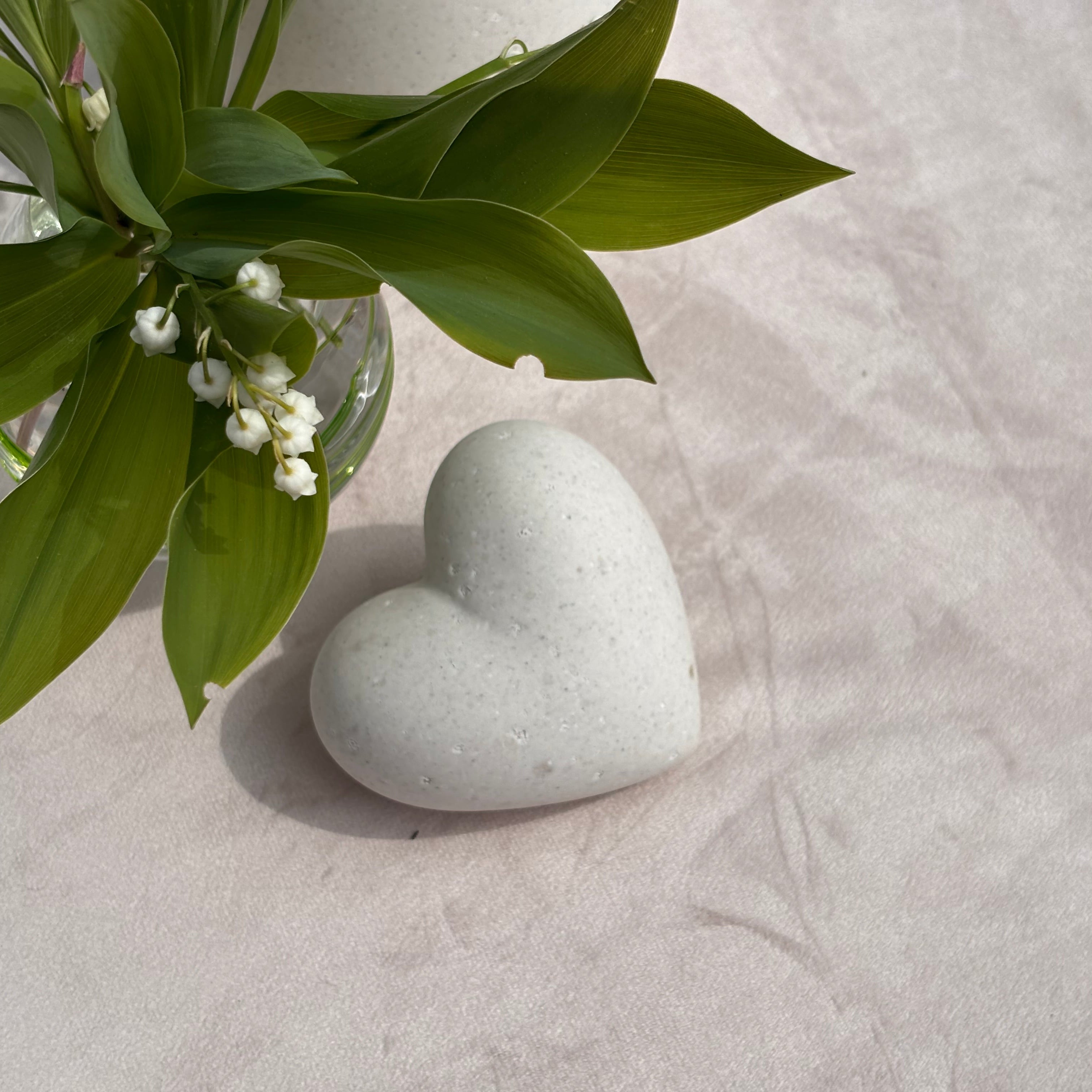 Heart-shaped stone on a textured surface with green leaves and small white flowers.